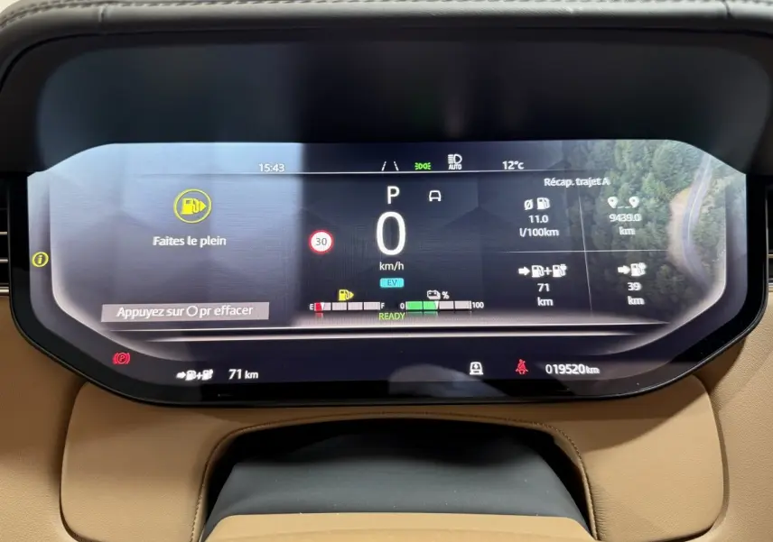 Tableau de bord numérique du Range Rover PHEV 2024 affichant vitesse, autonomie et alertes, vue frontale rapprochée.