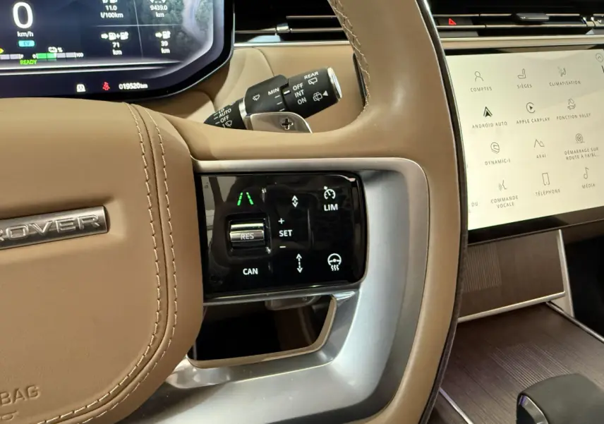 Gros plan sur le volant beige du Range Rover PHEV 2024 avec commandes tactiles et tableau de bord digital.