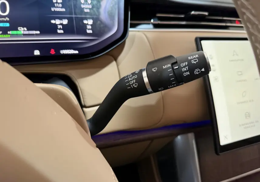 Gros plan sur la commande d’essuie-glace dans l’habitacle beige du Range Rover PHEV P550e noir, avec écran tactile visible.