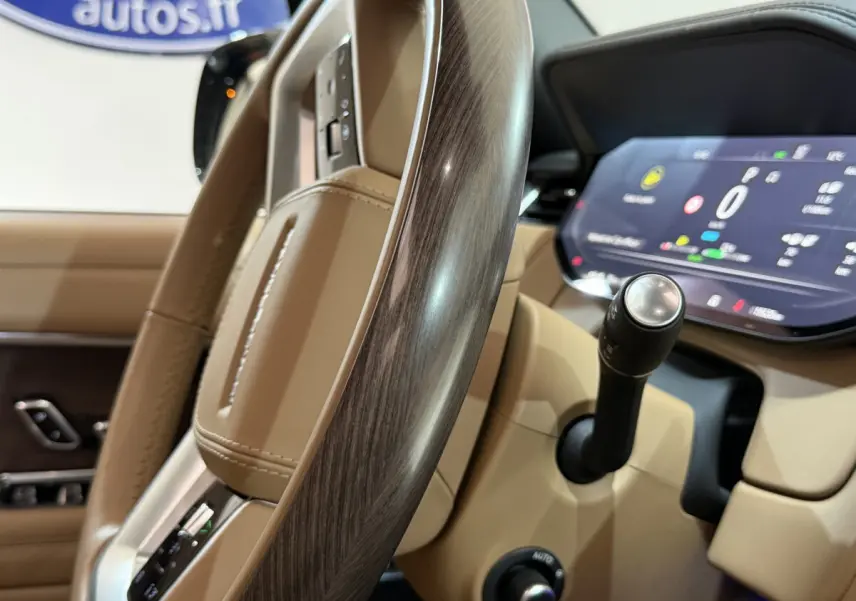 Gros plan sur le volant bois et cuir beige du Range Rover PHEV 2024 avec tableau de bord digital et levier de vitesses.