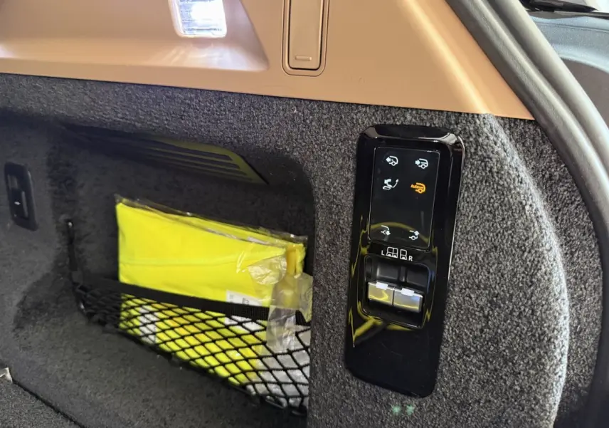 Détail du coffre du Range Rover PHEV noir 2024 montrant les commandes électriques et un gilet jaune rangé dans un filet.