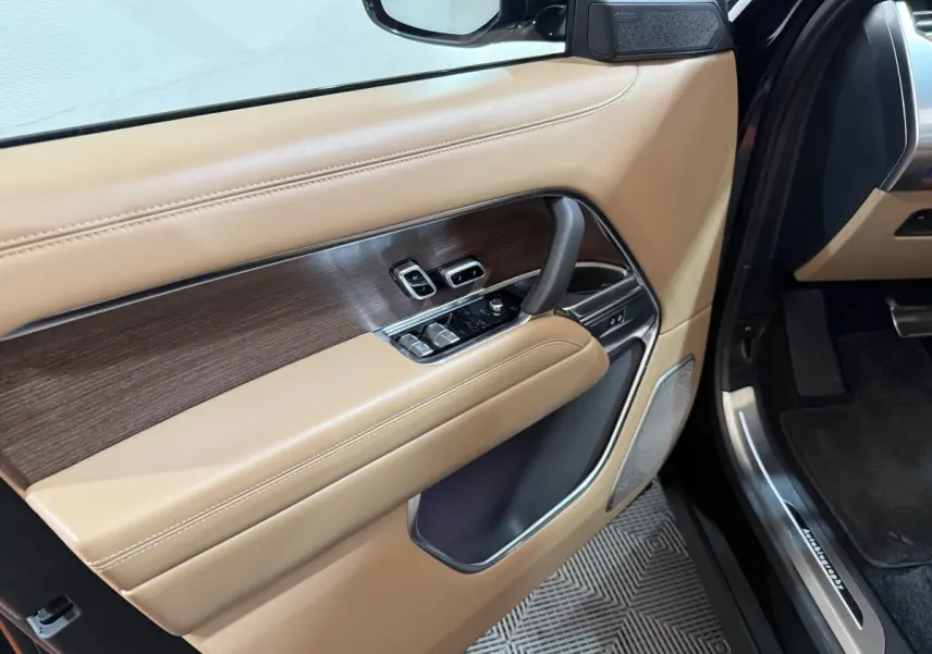 Vue intérieure côté gauche de la porte avant beige et bois du Range Rover PHEV 2024 avec commandes électriques et haut-parleur intégré.