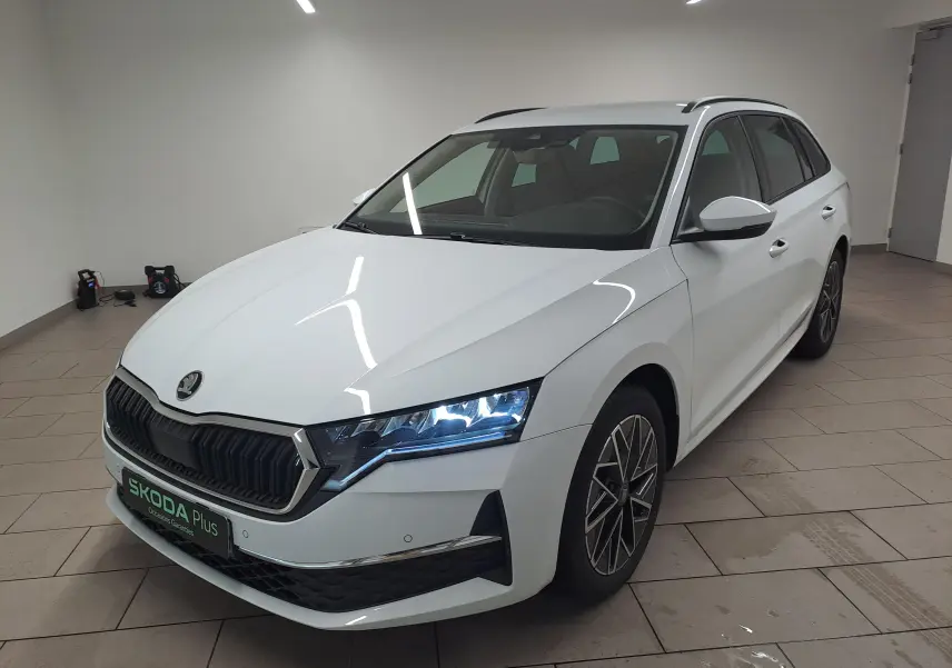 Vue 3/4 avant droite d'une Skoda Octavia Combi 2025 blanc Moon avec jantes alliage noires polies et phares LED allumés.