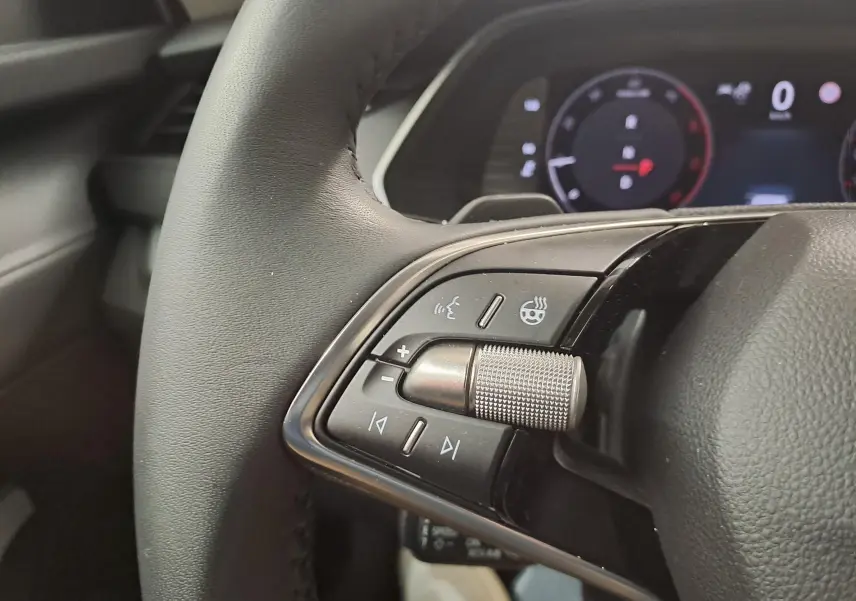 Gros plan sur la commande de volume et chauffage du volant cuir noir de la Skoda Octavia Combi 2025, tableau de bord en arrière-plan.