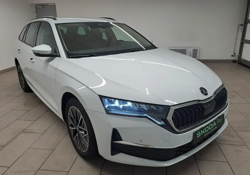 Vue 3/4 avant gauche d'une Skoda Octavia Combi blanche Moon avec phares allumés et jantes alliage noires polies.