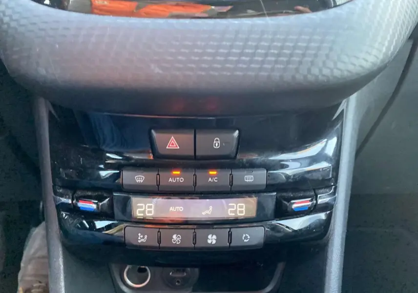 Gros plan sur la console centrale noire brillante du Peugeot 2008 avec commandes climatisation et bouton feux de détresse.