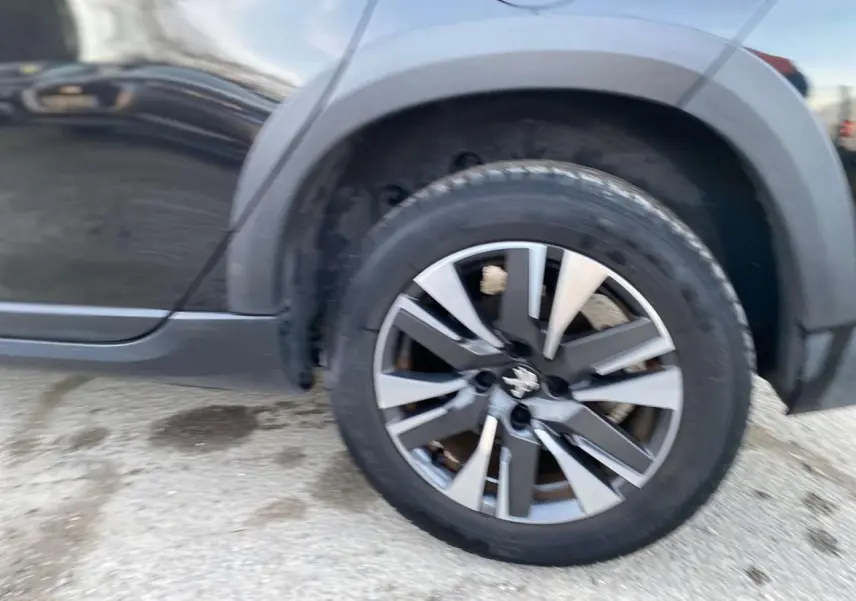 Gros plan sur la roue arrière droite d'une Peugeot 2008 noire Perla Nera avec jante aluminium diamantée.