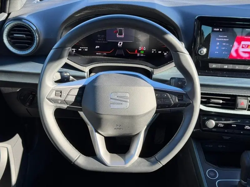 Vue intérieure centrée sur le volant du SEAT Arona 2025, avec tableau de bord numérique et écran tactile à droite.