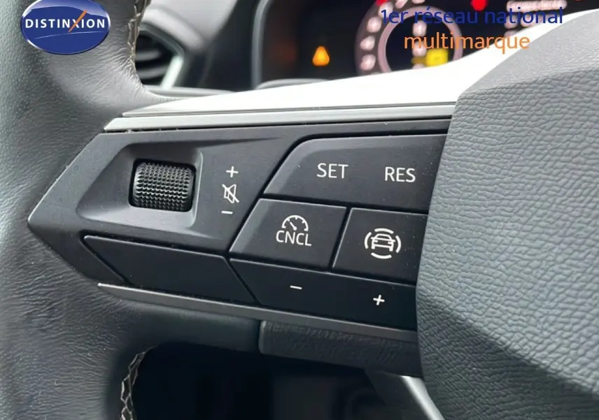 Gros plan sur les commandes au volant d’une SEAT LEON gris Fiord, mettant en valeur les boutons de régulateur de vitesse et volume.