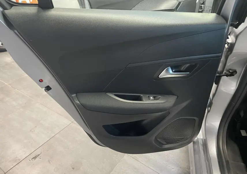 Vue intérieure de la porte avant gauche gris clair de la Peugeot 208 2024 avec commande de lève-vitre et haut-parleur intégré.