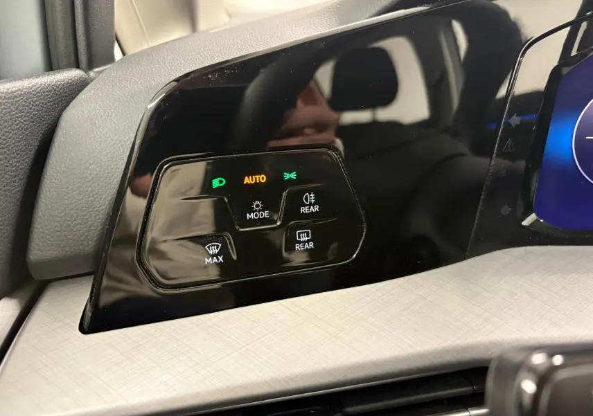 Gros plan sur les commandes d’éclairage et de désembuage du tableau de bord noir brillant d’une Volkswagen Golf 2025 couleur reflet d’argent.