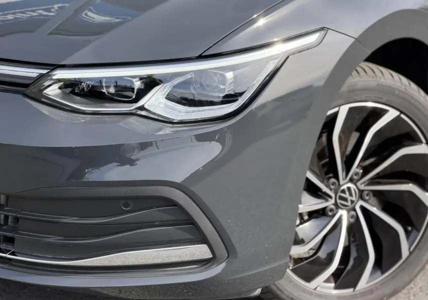 Gros plan sur l'avant droit de la Volkswagen Golf VIII gris Urano, mettant en valeur le phare LED et la jante alliage 17 pouces.