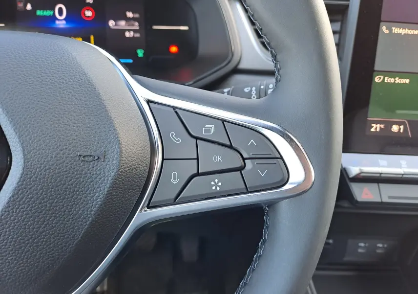 Gros plan sur les commandes au volant à droite du Renault Captur blanc nacré 2025, avec tableau de bord numérique en arrière-plan.