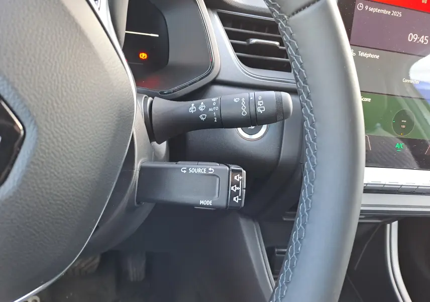 Gros plan sur la commande multifonction et le volant gris du Renault Captur 2025 hybride, avec tableau de bord numérique visible.