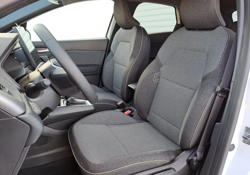 Intérieur avant droit du Renault Captur 2025, sièges tissu gris avec coutures contrastantes et volant visible.