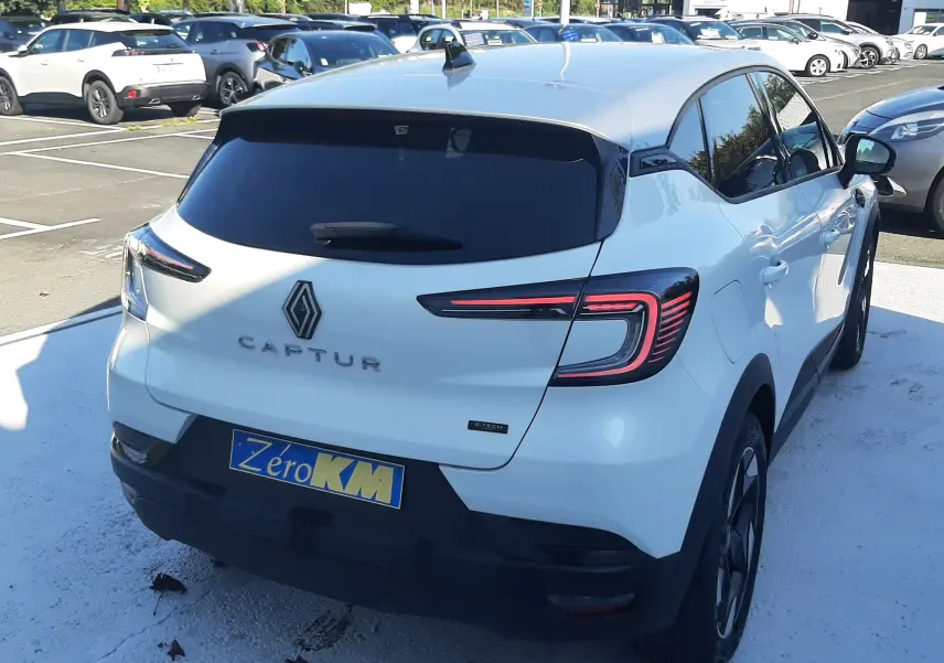 Vue 3/4 arrière droite d'un Renault Captur blanc nacré avec toit gris Highland, feux arrière LED distinctifs et plaque Zero KM.