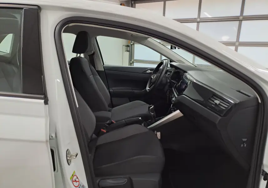 Intérieur côté conducteur d'une Volkswagen Polo blanc pur 2024, montrant les sièges noirs et le tableau de bord moderne.