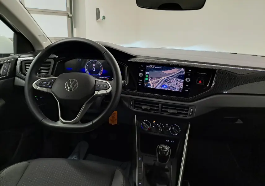 Vue intérieure avant du tableau de bord de la Volkswagen Polo blanche 2024 avec volant multifonction et écran tactile central.
