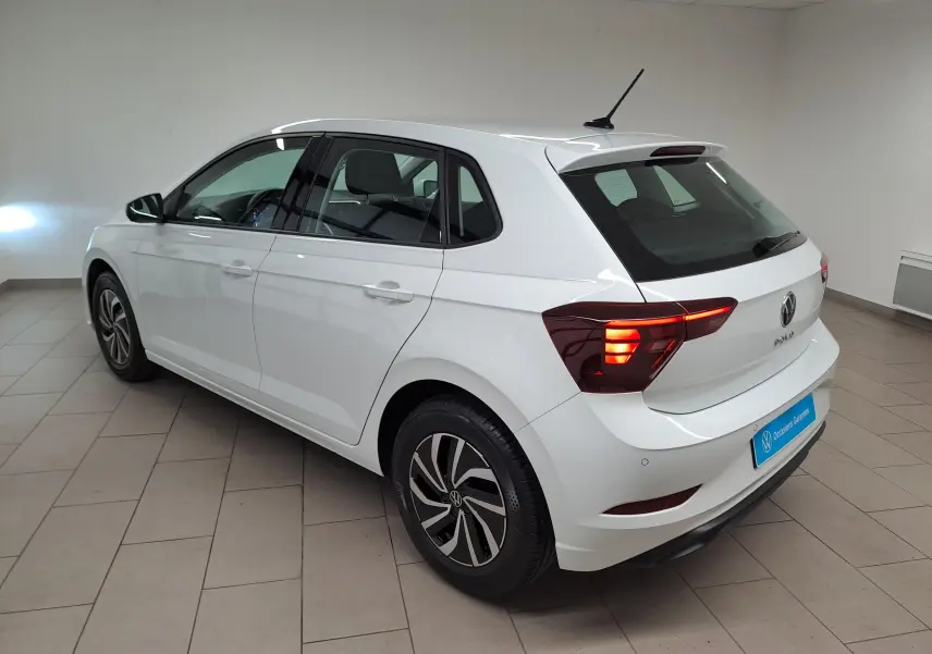 Vue 3/4 arrière droite d'une Volkswagen Polo blanche 2024 avec feux arrière allumés dans un intérieur neutre.