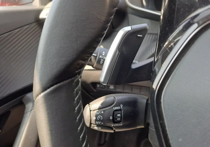 Gros plan sur la commande de régulateur de vitesse à gauche du volant en cuir noir du Peugeot 2008 rouge 2021.