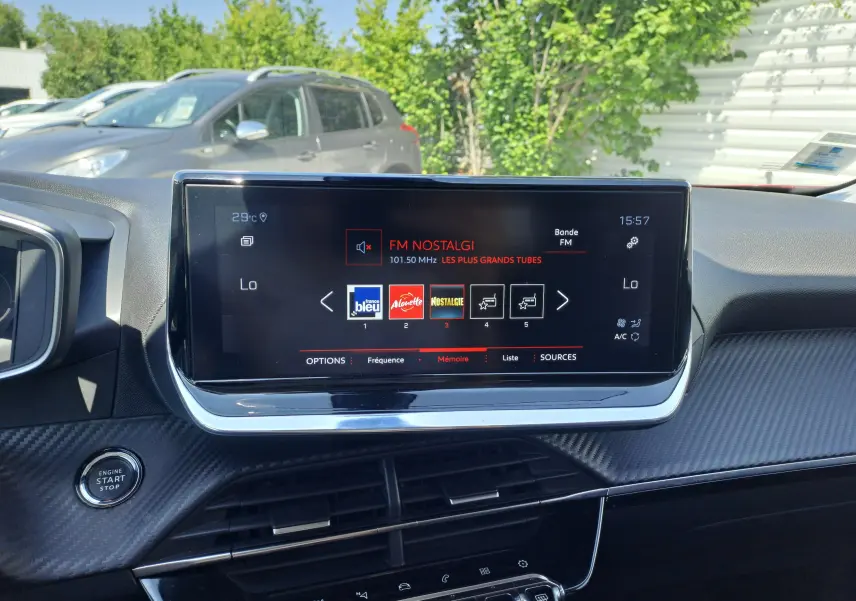 Écran central tactile du tableau de bord d’un Peugeot 2008 rouge, affichant la radio FM Nostalgie à 15h57.