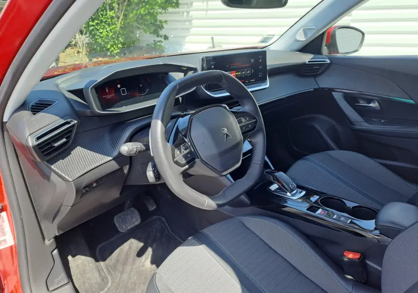 Intérieur de la Peugeot 2008 rouge vu côté conducteur, volant compact et tableau de bord numérique moderne.