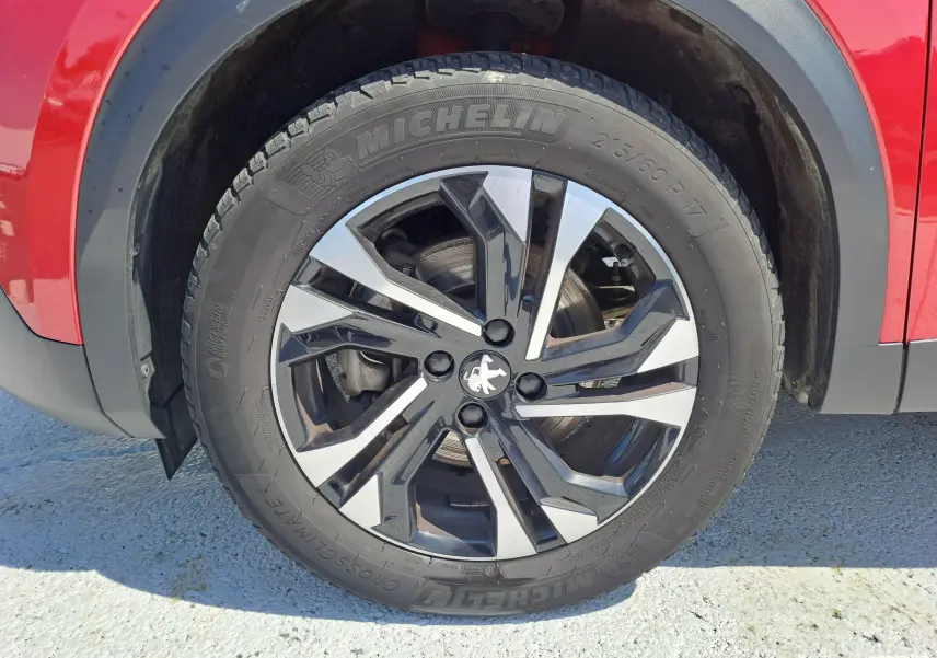 Gros plan sur la roue avant gauche du Peugeot 2008 rouge, mettant en valeur la jante alliage noire et argentée avec logo lion.