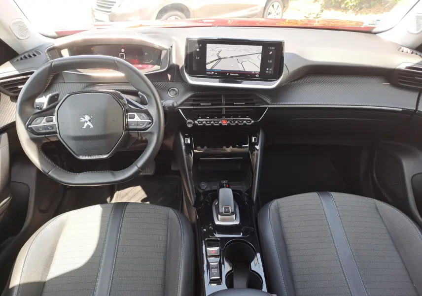Vue intérieure frontale du tableau de bord et volant noir du Peugeot 2008 rouge, avec écran tactile et console centrale moderne.