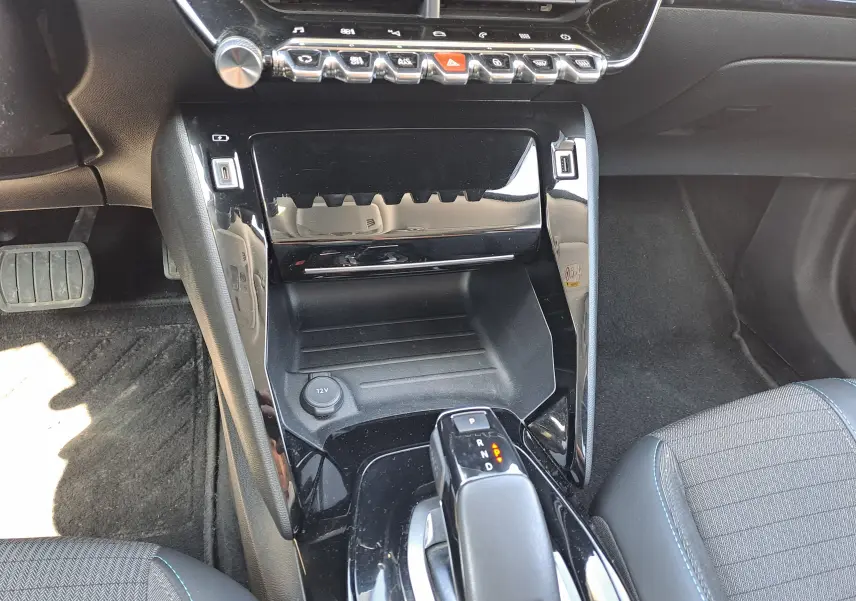 Vue rapprochée de la console centrale noire brillante du Peugeot 2008 rouge, avec levier de boîte auto et commandes tactiles.