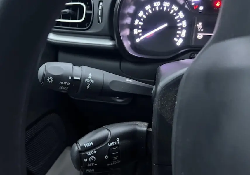 Gros plan sur les commandes au volant et le compteur lumineux d'une Citroën C3 Shine 2023 noir toit rouge.