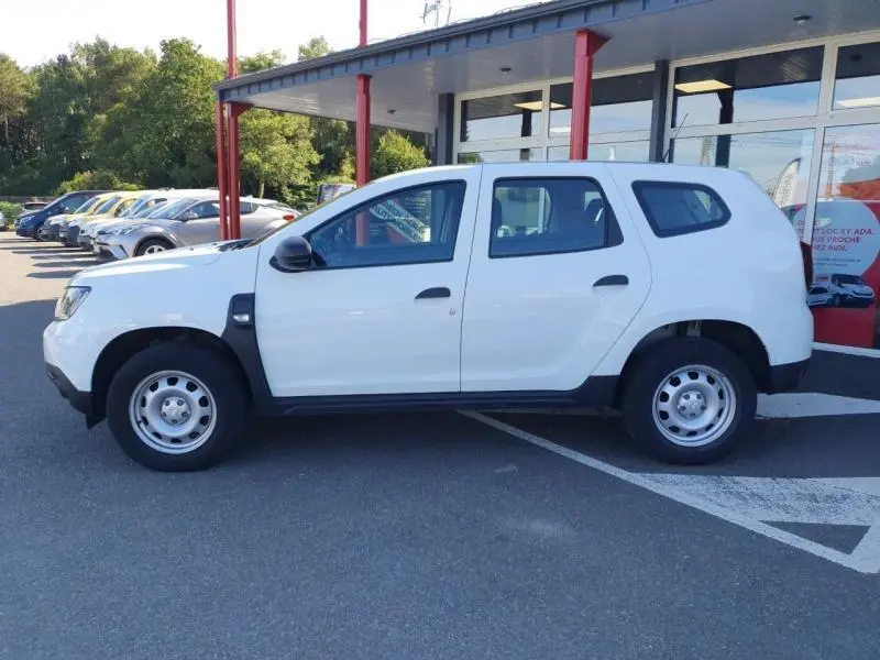 Profil côté gauche d'un Dacia Duster blanc Glacier 2021 avec jantes acier et rétroviseurs noirs, stationné devant un showroom.