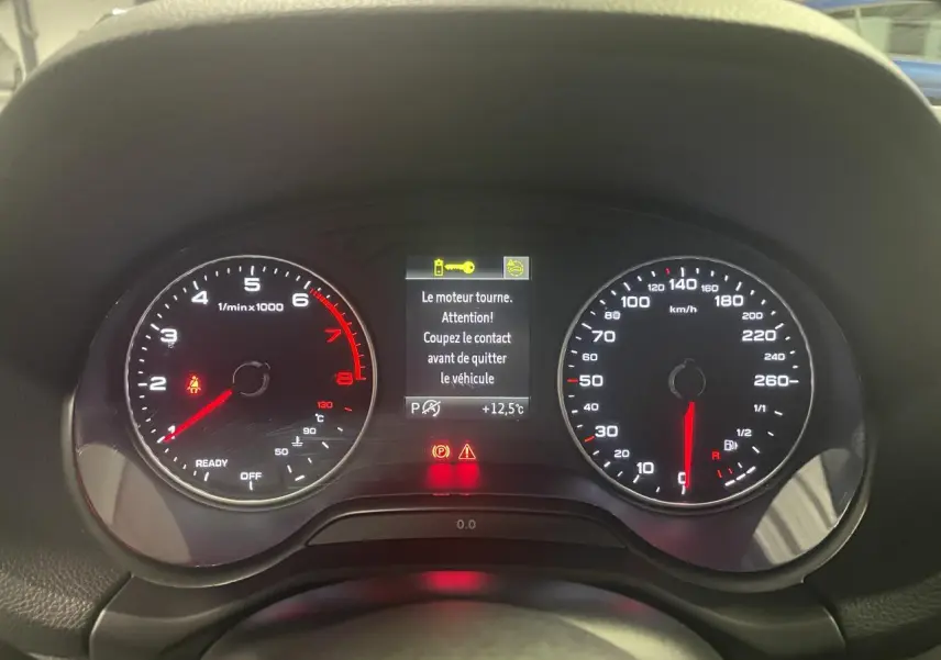 Vue frontale du tableau de bord de l'Audi Q2 noir, affichant compte-tours, vitesse et messages d'alerte au centre.