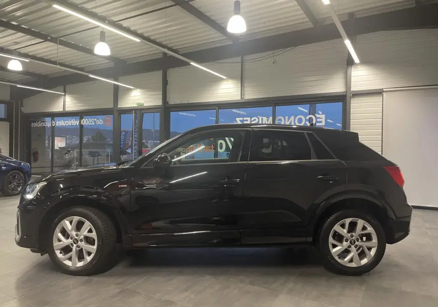 Vue de profil côté gauche d'un Audi Q2 noir métallisé S line avec jantes alliage en showroom.