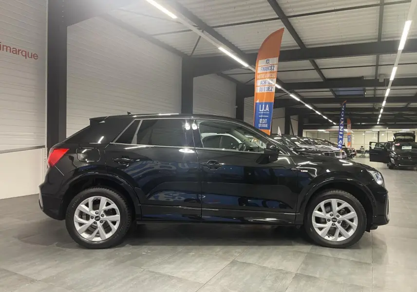 Audi Q2 noir métallisé vue de profil côté gauche dans un showroom avec jantes alliage et vitres surteintées.