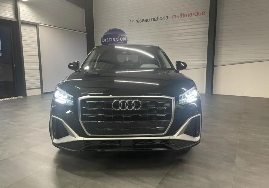 Audi Q2 S line noir métallisé vue de face avec phares Matrix LED allumés en intérieur showroom.