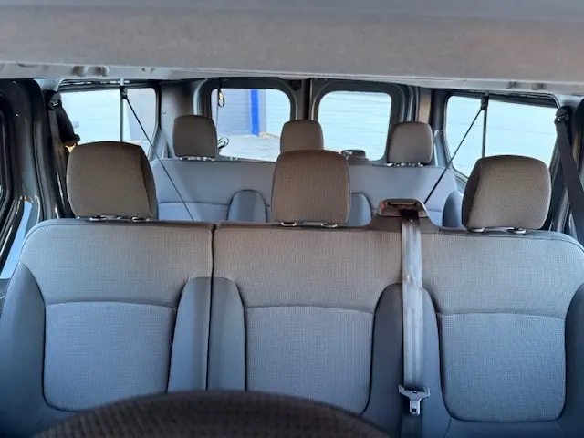 Vue intérieure arrière du Renault Trafic Fourgon gris clair 2025, montrant les trois rangées de sièges en tissu.