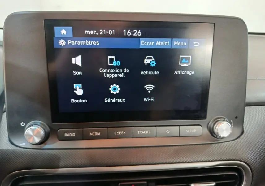 Écran tactile central allumé affichant les paramètres multimédia dans l'habitacle du Hyundai Kona bleu.