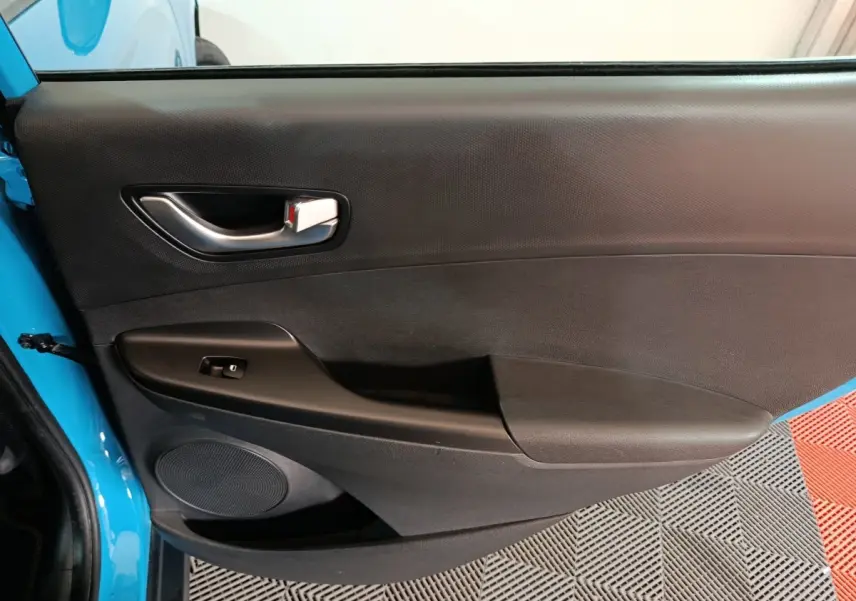 Vue intérieure de la porte avant gauche bleu électrique du Hyundai Kona BEV avec poignée argentée et commande de vitre.