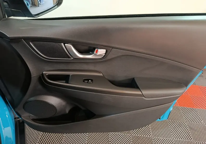 Intérieur côté conducteur de Hyundai Kona électrique bleu 2022, porte avec poignée argent et commande fenêtre noire.