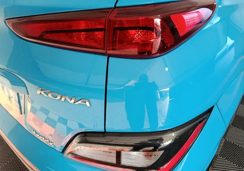 Gros plan sur le feu arrière droit et le logo KONA d’une Hyundai Kona électrique bleue, vue arrière côté droit.