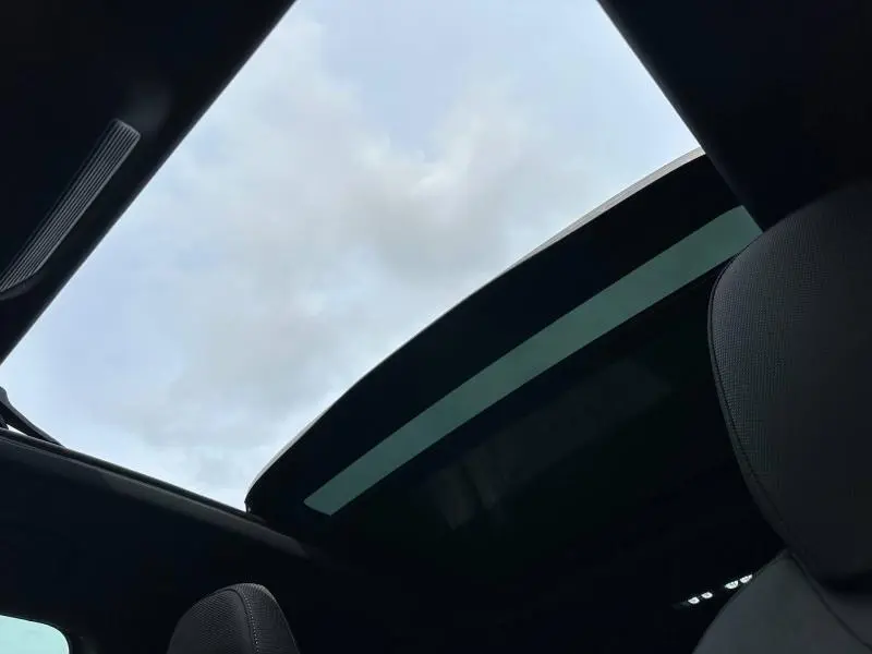 Toit ouvrant panoramique ouvert vu de l'intérieur sur un Audi Q3 Noir Mythique métallisé, ciel nuageux en arrière-plan.