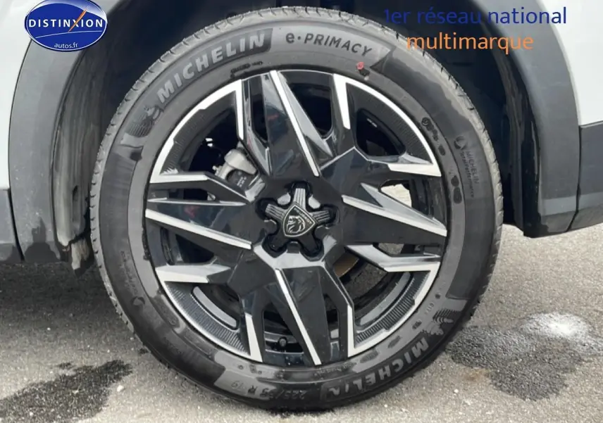 Gros plan sur la roue avant gauche d’un Peugeot 3008 blanc, jante alu noire et argent avec logo lion central.