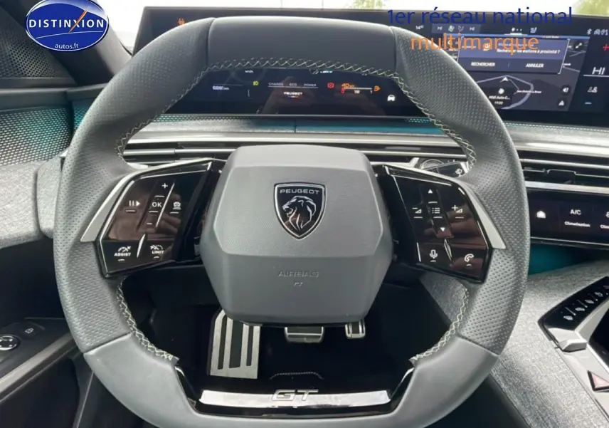 Volant cuir multifonction vu de face dans un Peugeot 3008 blanc 2025, avec logo et pédalier sport visibles.