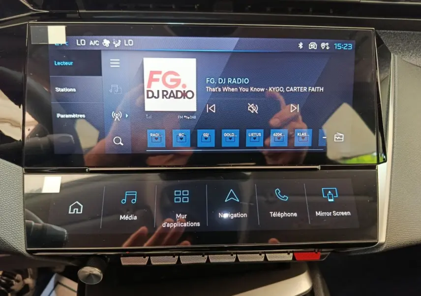 Écran tactile central de la Peugeot 308 gris foncé, affichant la radio FG DJ Radio en intérieur.