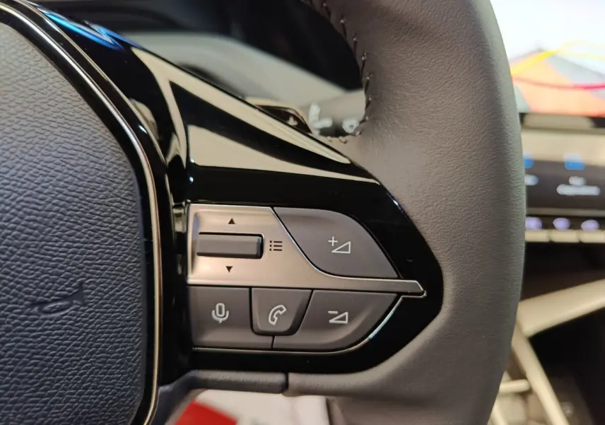 Gros plan sur le volant cuir gris foncé de la Peugeot 308 2026, avec commandes multifonctions visibles.