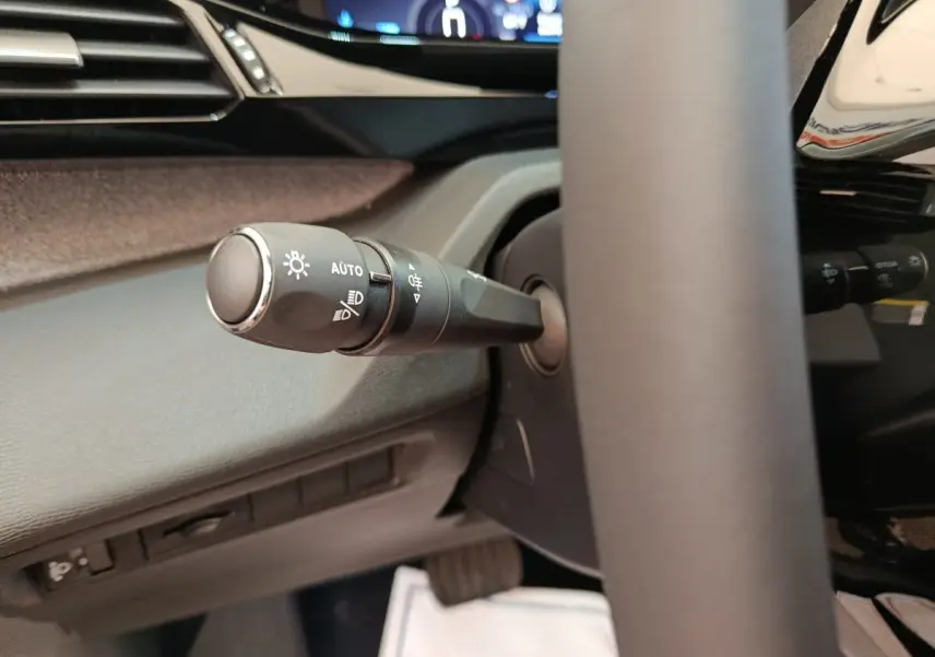 Gros plan sur la commande des phares à gauche du volant cuir dans l’habitacle gris foncé de la Peugeot 308 2026.