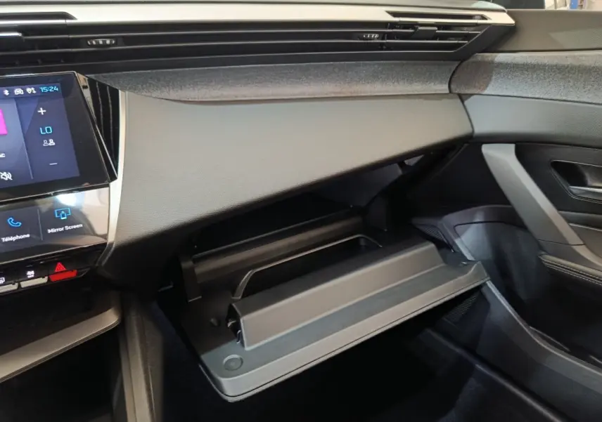 Intérieur de la Peugeot 308 2026 gris foncé, vue côté passager sur la boîte à gants ouverte et tableau de bord moderne.