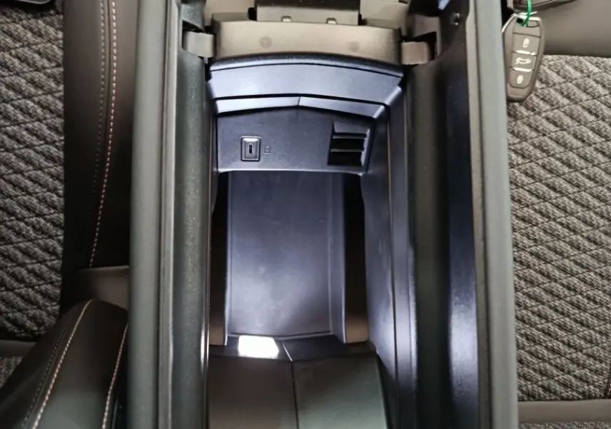 Vue plongeante sur l'accoudoir central ouvert de la Peugeot 308 gris foncé, avec clé et port USB visibles.