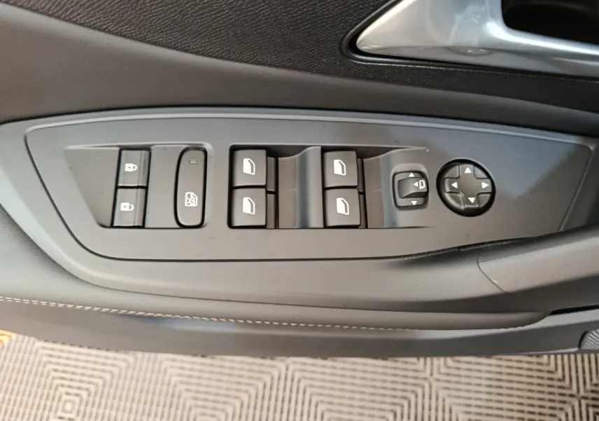 Gros plan sur les commandes de lève-vitres et réglages des rétroviseurs côté conducteur d’une Peugeot 308 gris foncé 2026.
