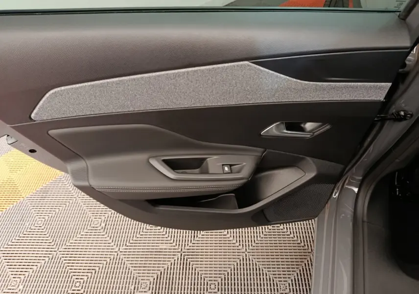 Vue intérieure de la porte avant droite gris foncé de la Peugeot 308 2026 avec insert tissu clair et commande de vitre.